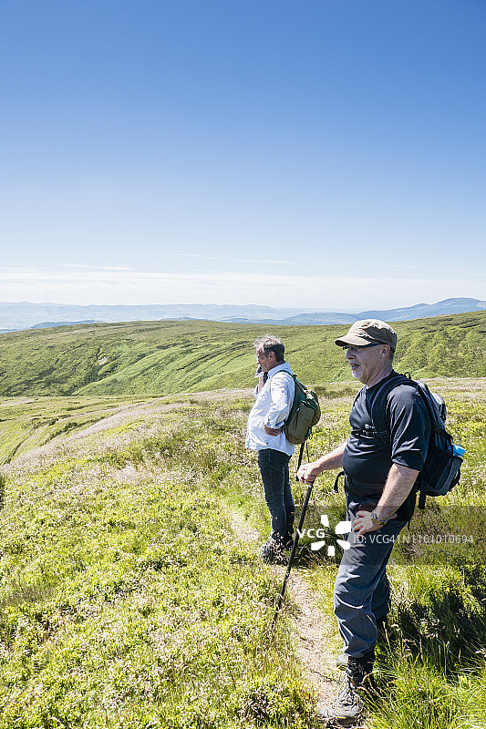 两名中年白人男性背包客在英国威尔士 Dinas Mawddwy 和 Bwlch Llyn Bach 之间的 Cambrian Way 观看山谷景色图片素材