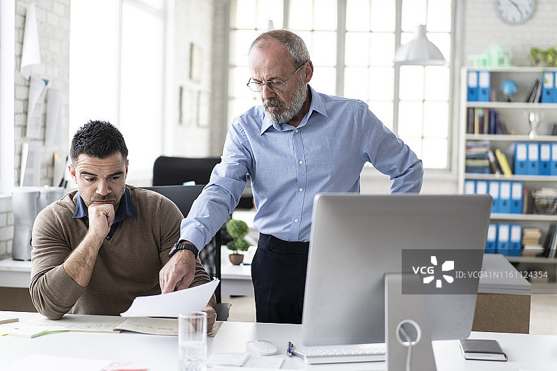 年长的经理向同事讲解电脑上的内容图片素材