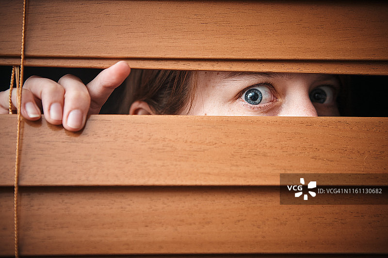 透过木制百叶窗窥视的惊恐年轻女人图片素材