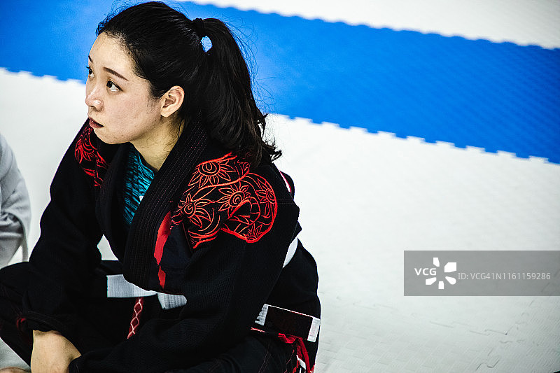 亚洲女性坐在道场垫子上，身穿柔术道服图片素材