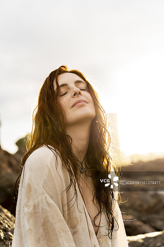 逆光下，鼻子上戴着鼻环的红发年轻女人肖像图片素材