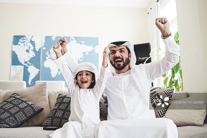 阿拉伯男子和他的儿子在家观看体育赛事图片素材