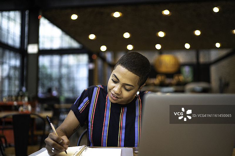 年轻女人在餐厅使用笔记本电脑，并在笔记本上写作图片素材