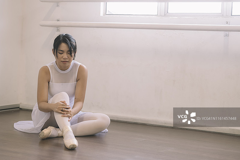 在芭蕾舞工作室练习时腿部受伤，坐在地上痛苦的亚洲少女图片素材