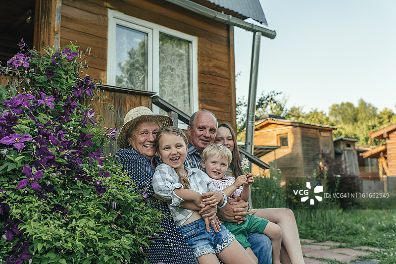 夏日里，祖父母和孙子孙女坐在房子旁图片素材