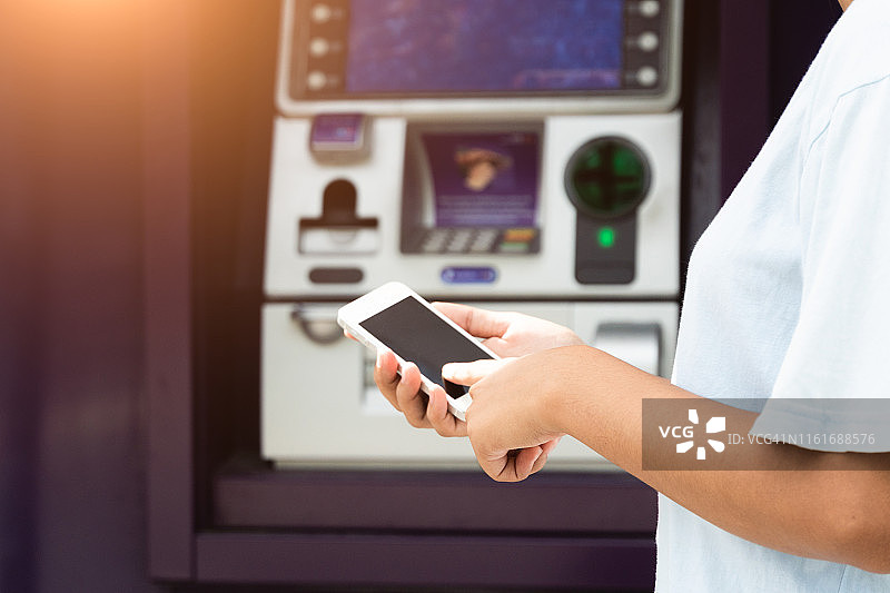 商务概念： woman在ATM前使用手机取款图片素材