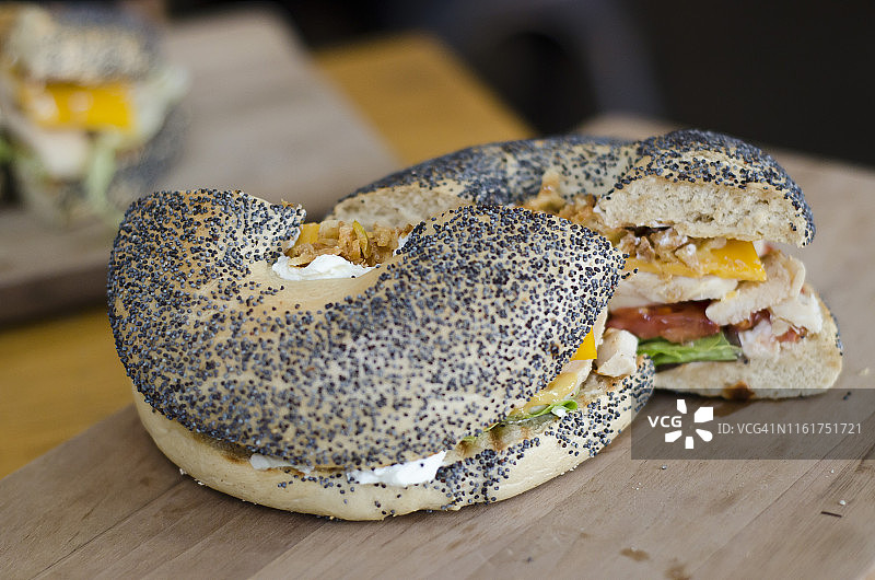 芝麻籽贝果汉堡配鸡肉、奶油奶酪、番茄和生菜，放在砧板上图片素材