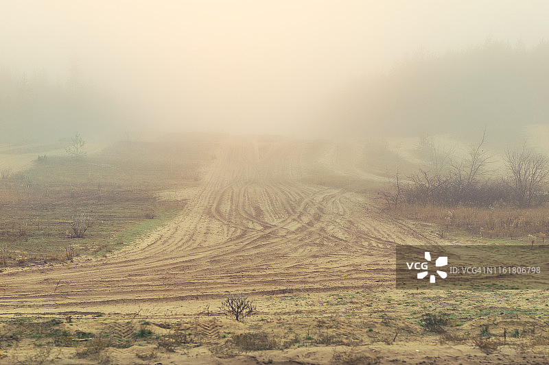 秋日清晨笼罩在浓雾中的神秘沙土路图片素材