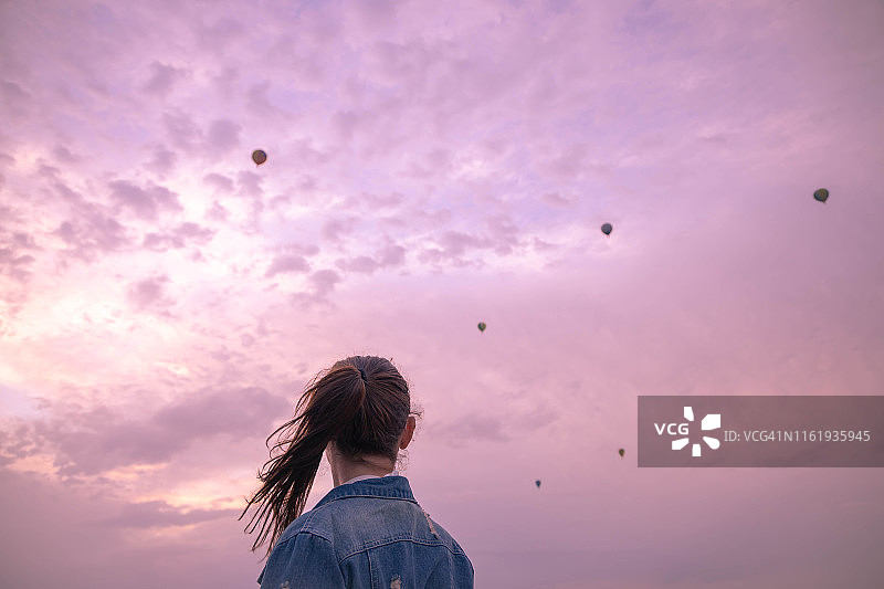 女人观看天空中飞行的热气球图片素材