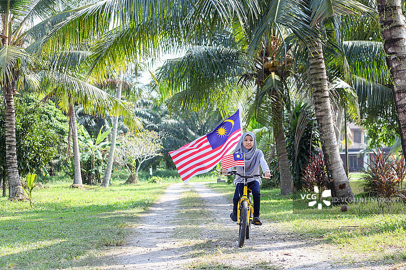 骑着挂着马来西亚国旗的自行车的马来西亚穆斯林女孩图片素材