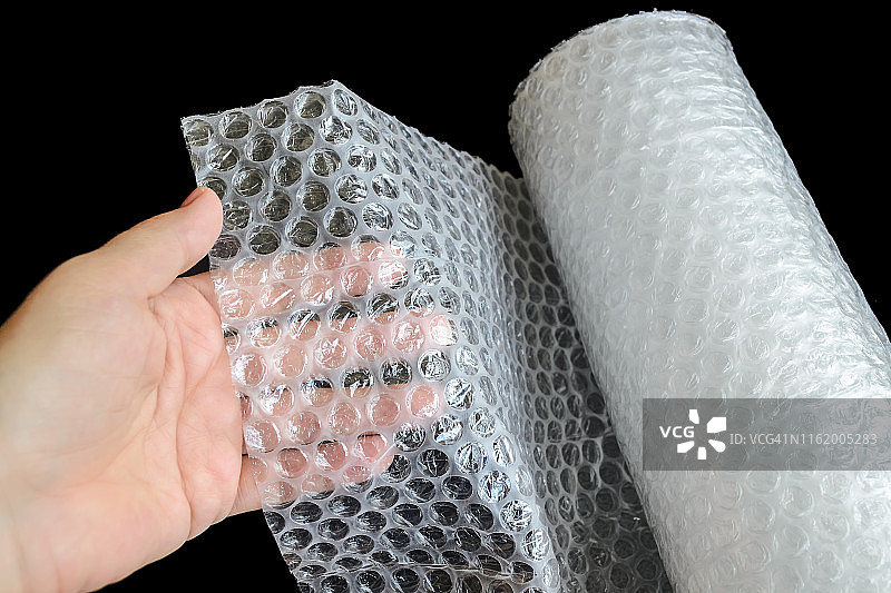 女人手在黑色背景上握着白色透明气泡膜。用于包装易碎物品以安全运输的材料。图片素材