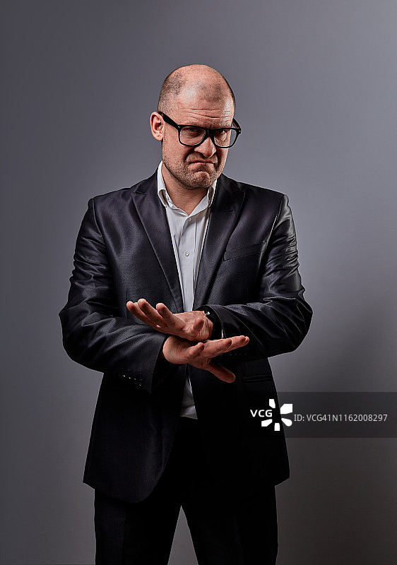 穿着黑色西装和眼镜的不快乐的男人在灰色背景上显示拒绝标志的棕榈图片素材