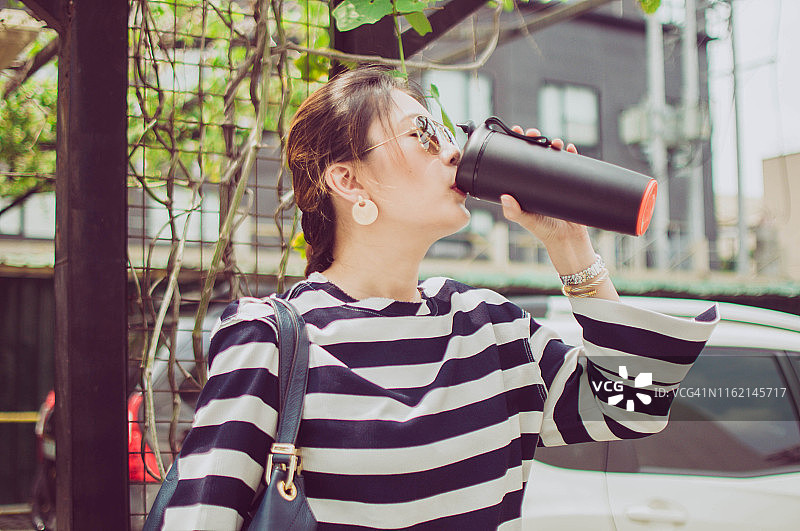 年轻美丽的亚洲女人正在用可重复使用的保温容器喝水图片素材