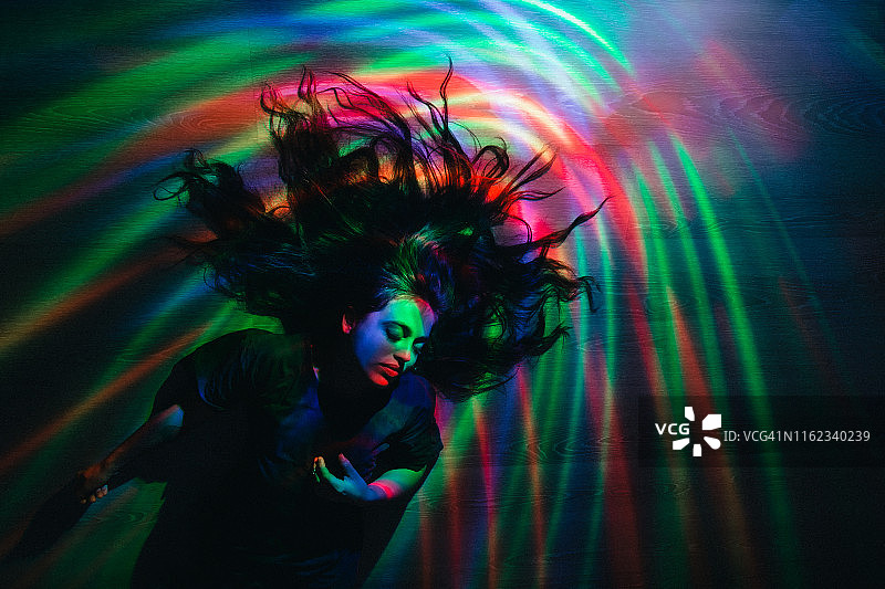 女孩躺在地板上，彩色灯光照耀着她图片素材