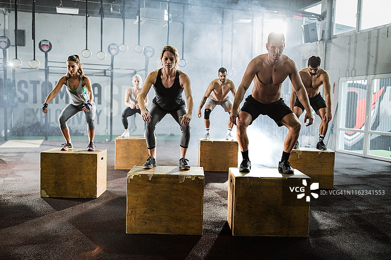 在健身房训练期间，健壮的人在板条箱上跳跃图片素材