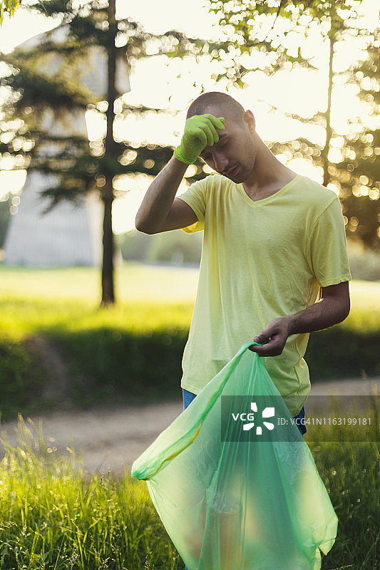 疲惫的年轻男子在公园里捡垃圾图片素材