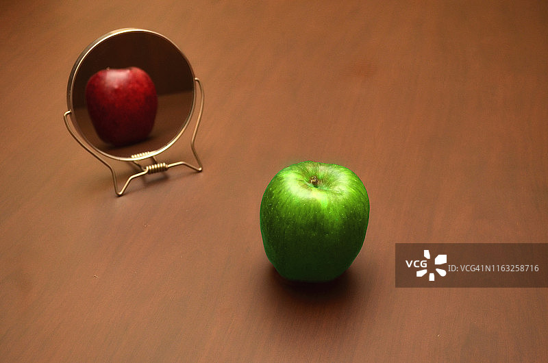 绿苹果在红镜子中显现真实倒影，展现真实与表象的差异图片素材