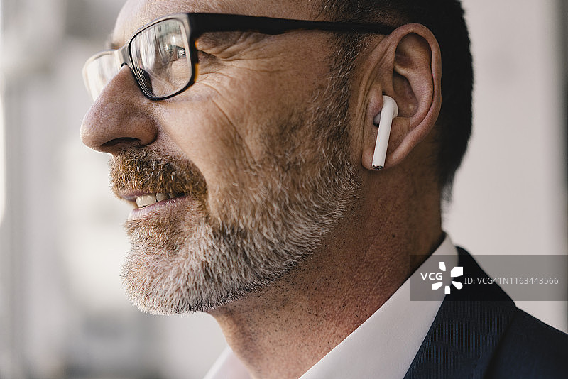 戴着蓝牙耳机听音乐的年长的商人肖像图片素材