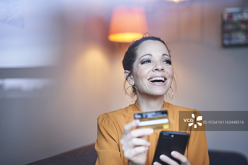 在家使用智能手机和信用卡的快乐女人图片素材