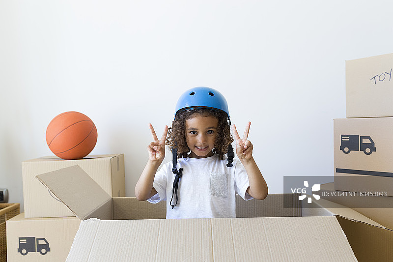 戴着自行车头盔，在新家纸箱外观望的女孩肖像图片素材