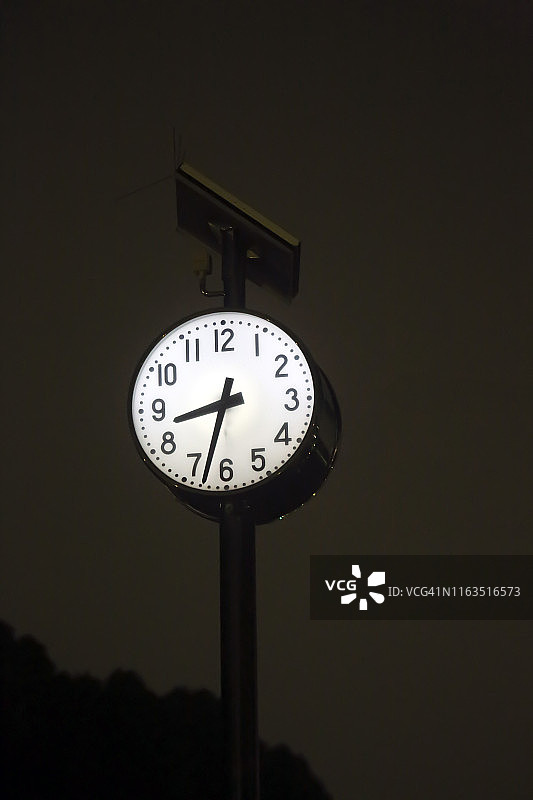 雨夜中，杆子上内部照明的时钟图片素材