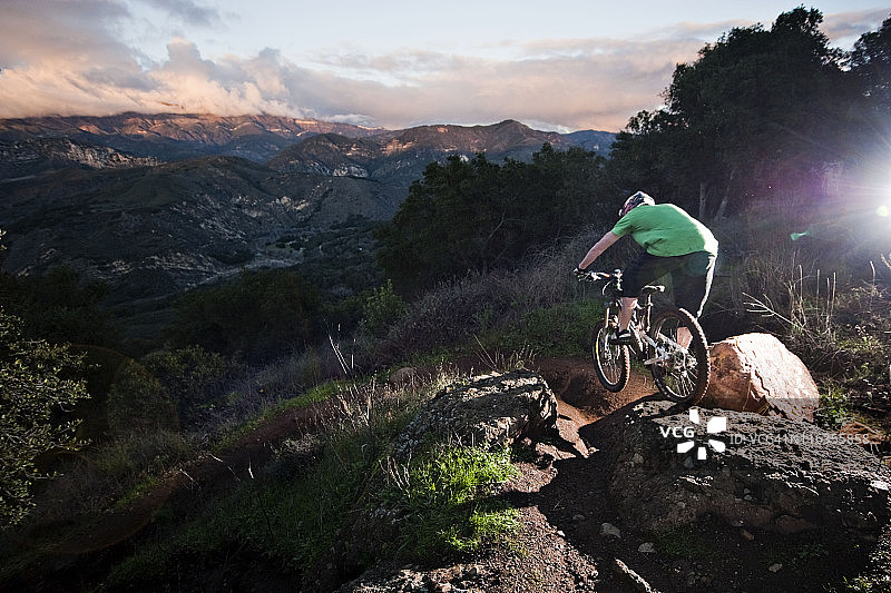 在加州圣巴巴拉，一位年轻人骑着速降山地自行车在纳普斯城堡小径上，周围环绕着美丽的景色图片素材