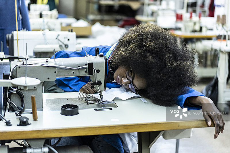 在缝纫机旁揉搓太阳穴的黑人妇女图片素材