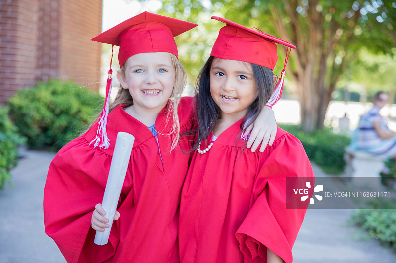 小学毕业典礼后，戴着毕业帽和礼服的女孩们在学校外微笑图片素材