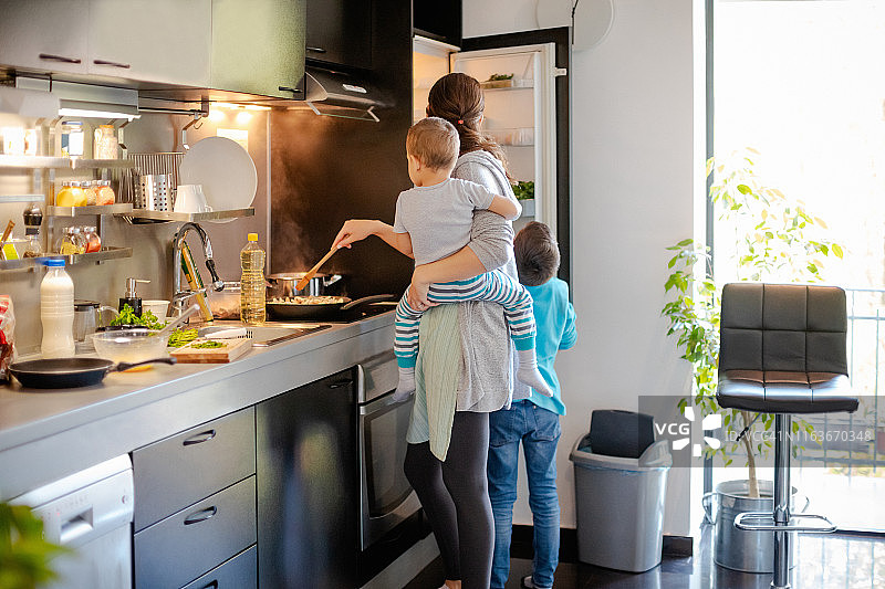 母亲和幼儿一起做饭，大儿子打开冰箱图片素材