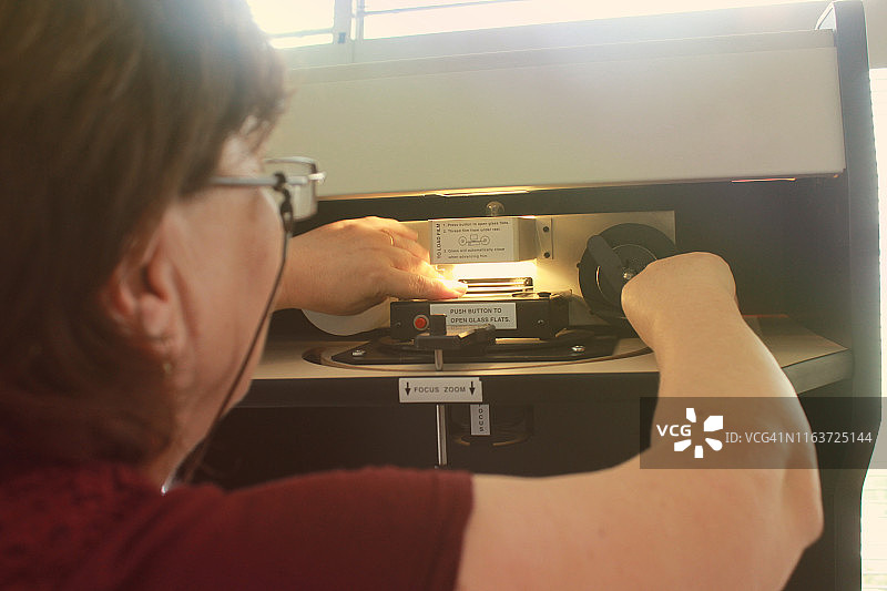 准备缩微胶片阅读器的老年女图书管理员图片素材