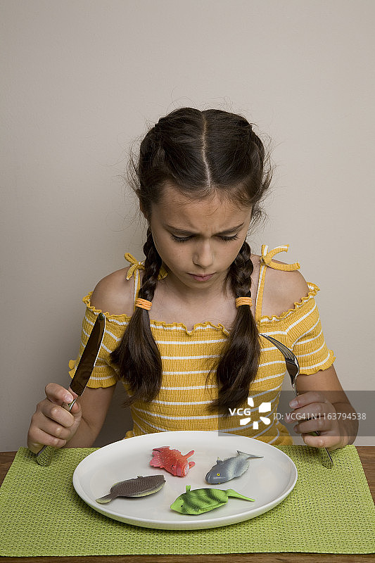 女孩坐在桌旁，盘子里放着塑料鱼图片素材