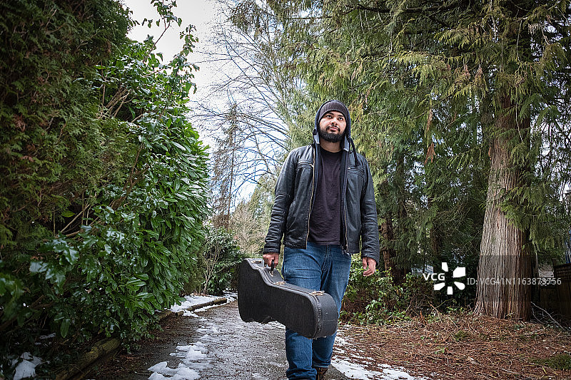 携带吉他盒走在雪地上的拉丁裔青年图片素材