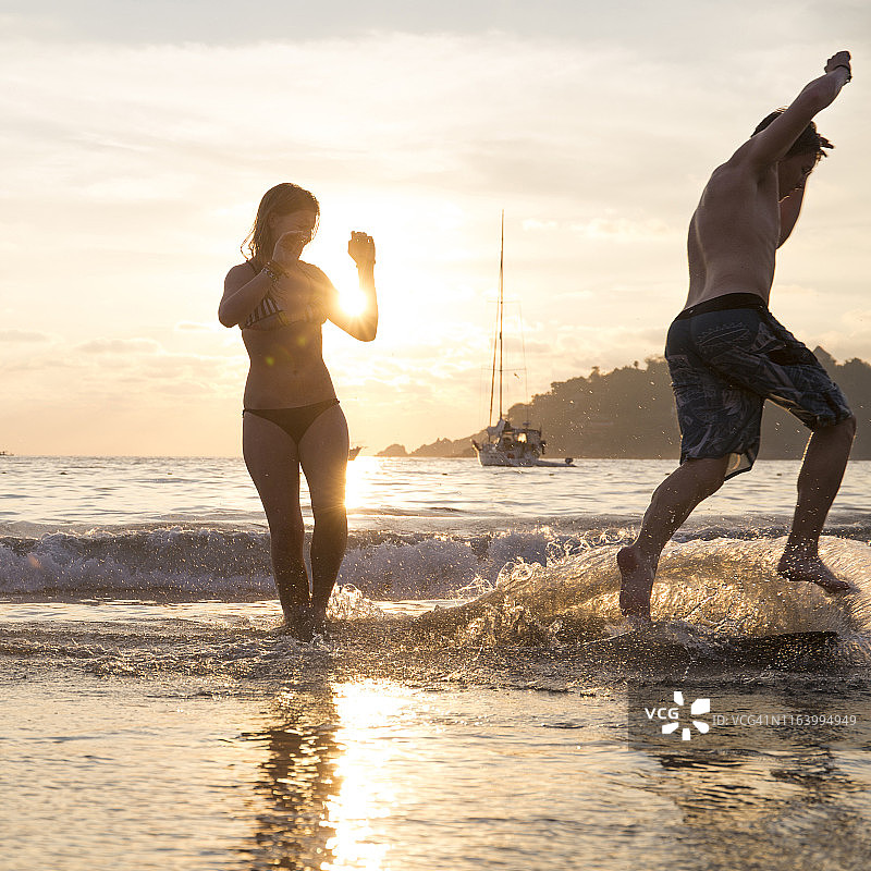 年轻女子和男人在日落时分的海滩上玩滑板图片素材