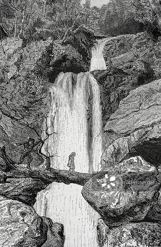 女孩走过危险的瀑布，身后跟着一个男人图片素材