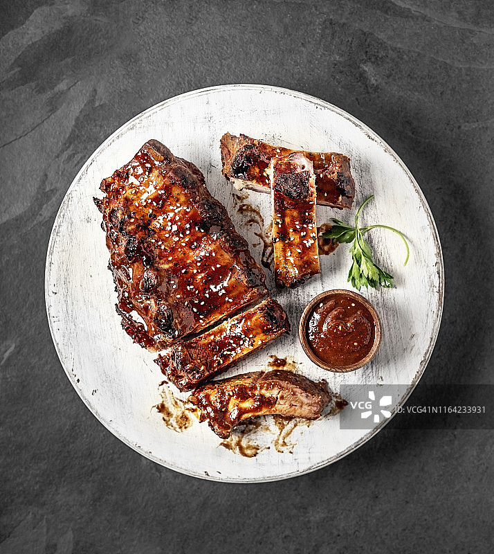 黑背景砧板上，一排烤制的全肋排配烧烤酱图片素材