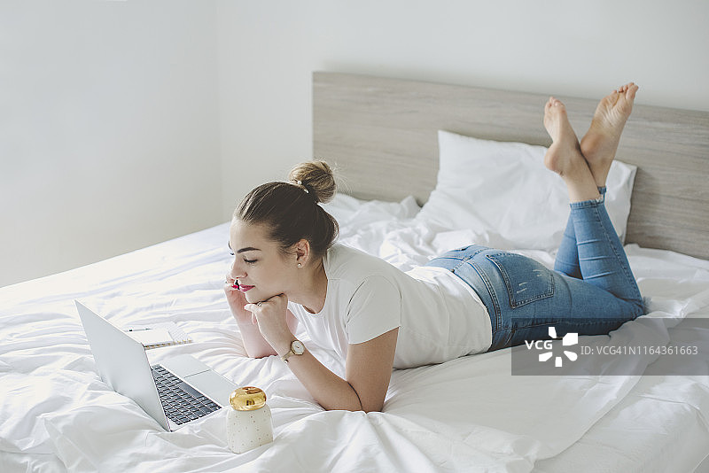 年轻女人在卧室里使用笔记本电脑工作图片素材