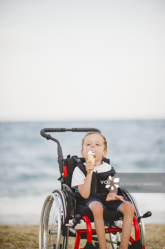 坐轮椅的小男孩在海边吃冰淇淋图片素材