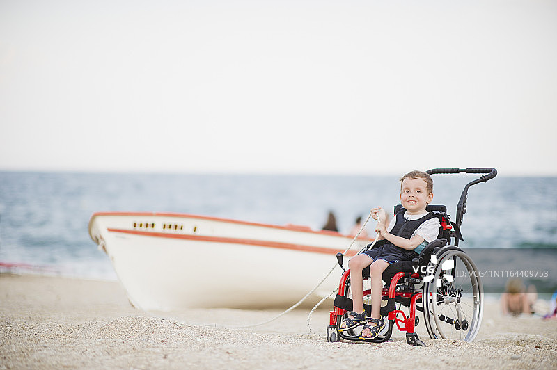 坐在轮椅上的可爱小男孩在海边图片素材
