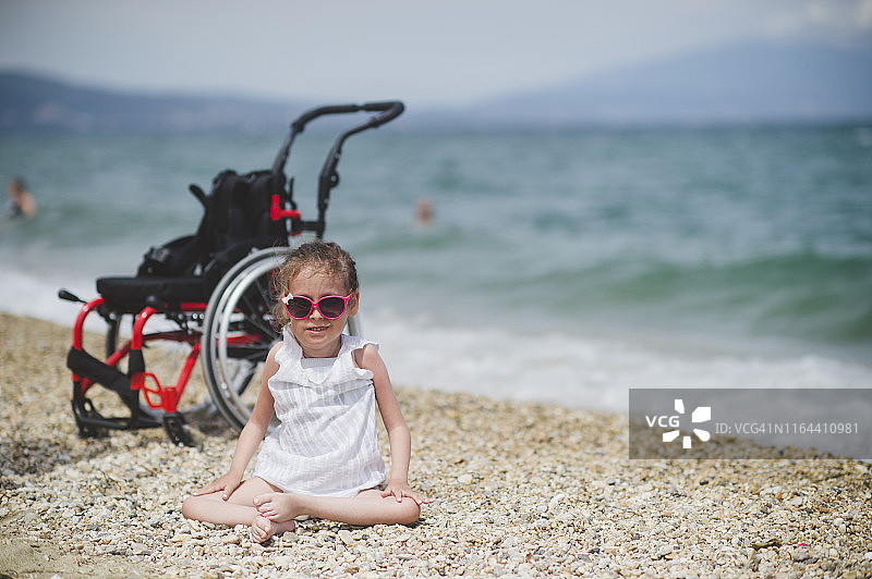 可爱的小女孩坐在海滩的轮椅旁图片素材