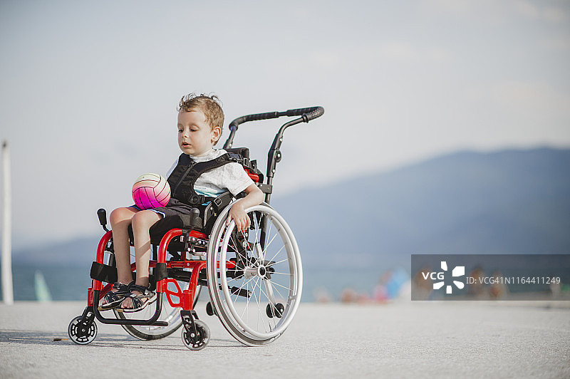 坐在轮椅上在海边的可爱小男孩图片素材