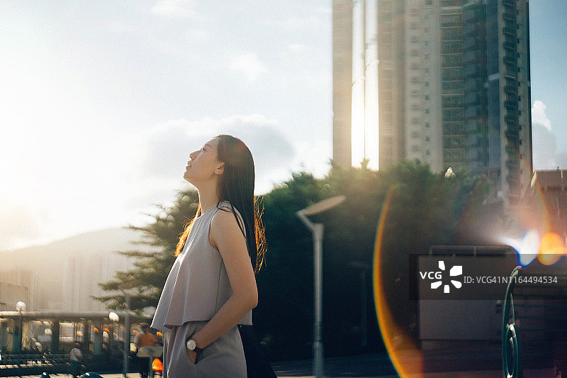 年轻亚裔女性在日落时分于城市中若有所思地仰望天空图片素材