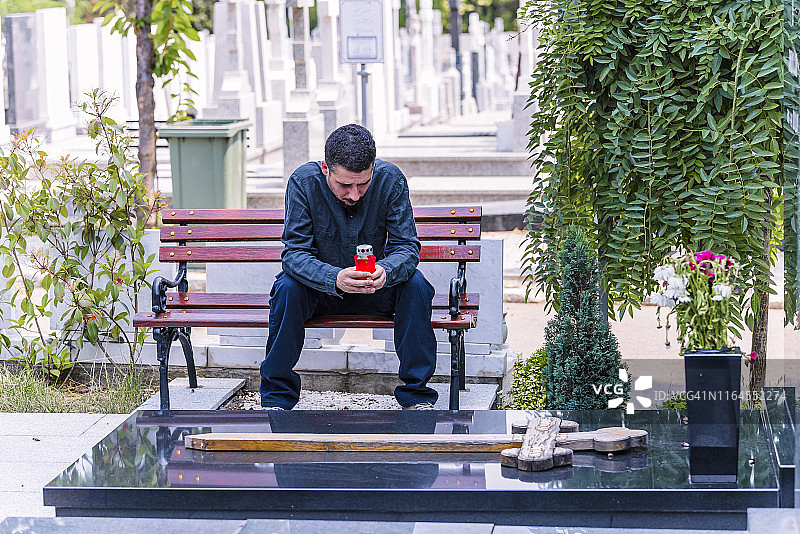 男子坐在墓地旁，点着红色蜡烛图片素材