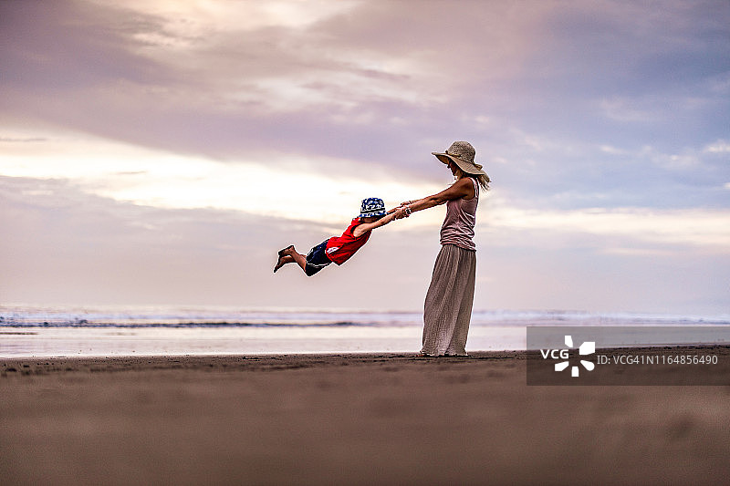 快乐的母亲在海滩上旋转她的儿子图片素材