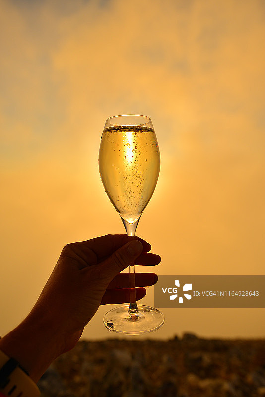 女人手持香槟酒杯，背景为日落图片素材