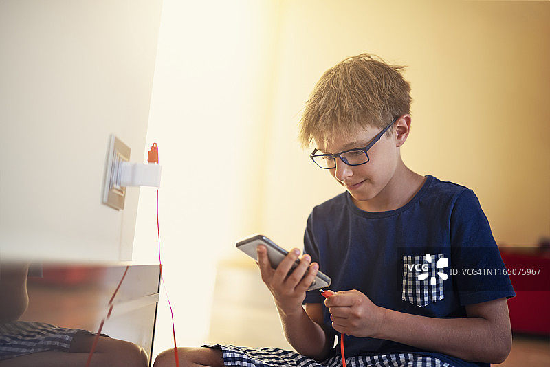 小男孩在家将智能手机连接到充电器图片素材