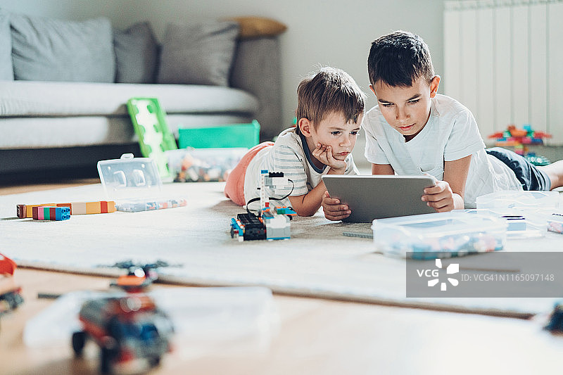 两个兄弟在地板上玩数字平板电脑和塑料积木图片素材