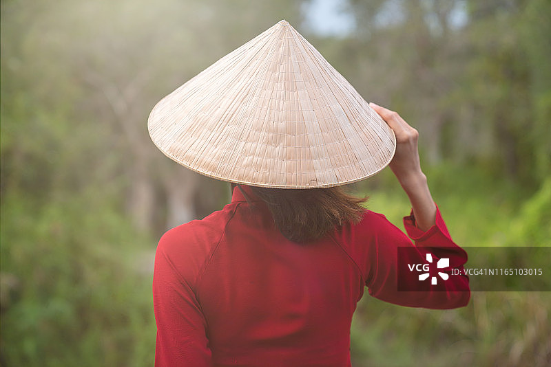 戴着越南斗笠、手捧莲花的亚洲女孩站在桥上图片素材