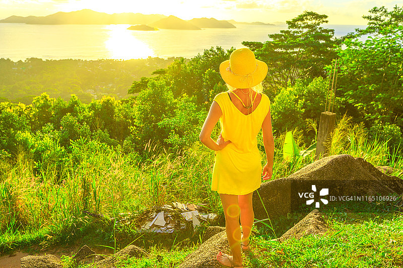 身穿黄色连衣裙的女游客在塞舌尔普拉兰岛欣赏日落美景图片素材