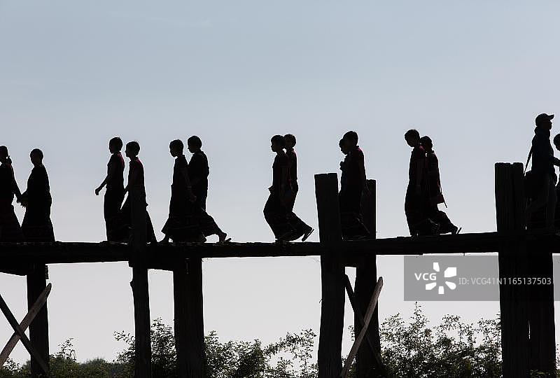 缅甸东塔曼湖乌本桥上的年轻佛教见习僧侣剪影图片素材