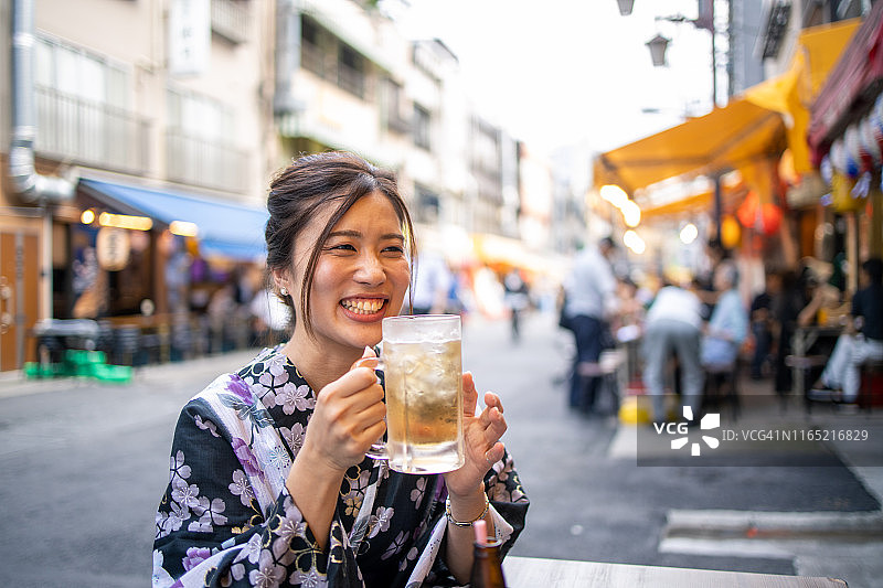 身穿浴衣，在下午户外喝啤酒的快乐年轻女人图片素材